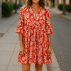 Woman wearing a red and beige floral tiered button dress from SageBay & Co walking on a city street