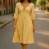 Woman wearing a yellow and white striped midi dress with a tie-front neckline from SageBay & Co, walking down a sunlit street