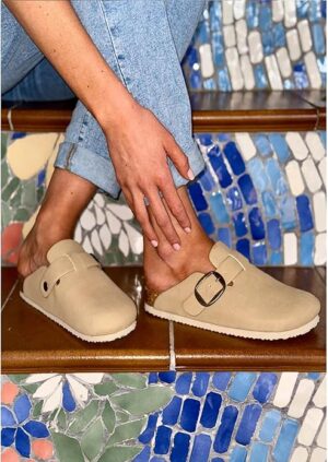 Woman wearing faux suede stone mules styled with rolled jeans on mosaic stairs