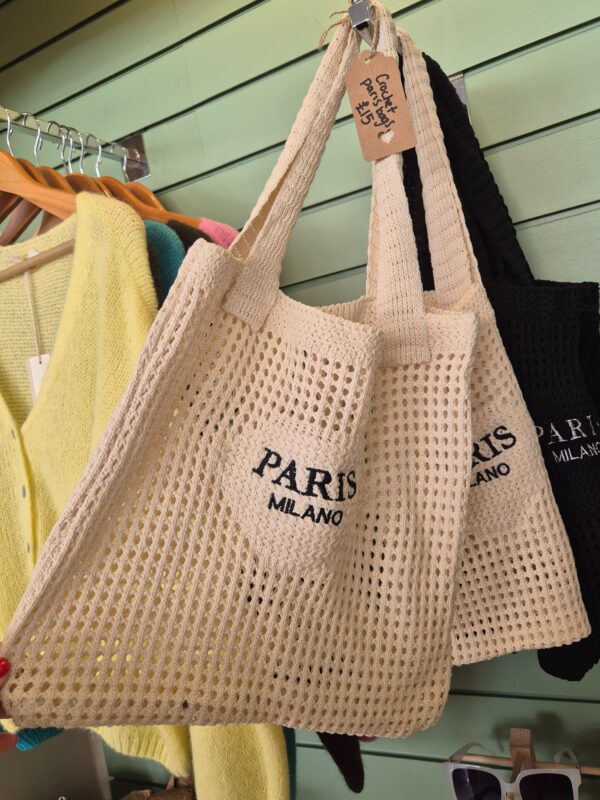 Cream crochet shoulder bag with “Paris Milano” embroidery hanging in a boutique
